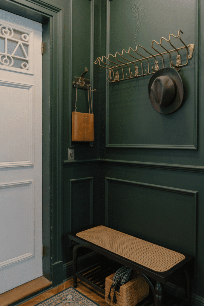 Moody green accent wall with brass hooks offers dramatic style and function in a small entry.