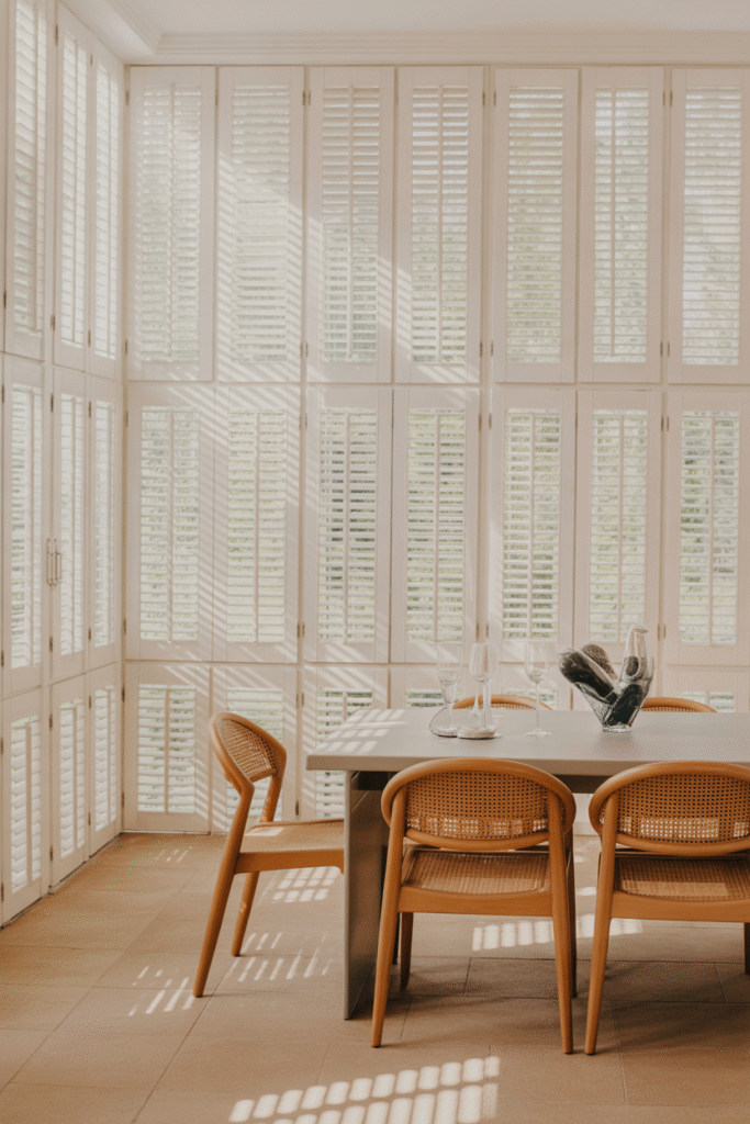 White floor to ceiling shutters in a bright dining room setting.